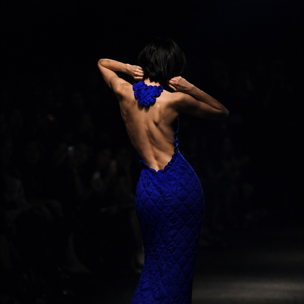 A woman in a dark blue dress in a moody editorial portrait.